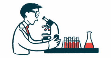 A researcher looks into a microscope near a rack of vials and a beaker.